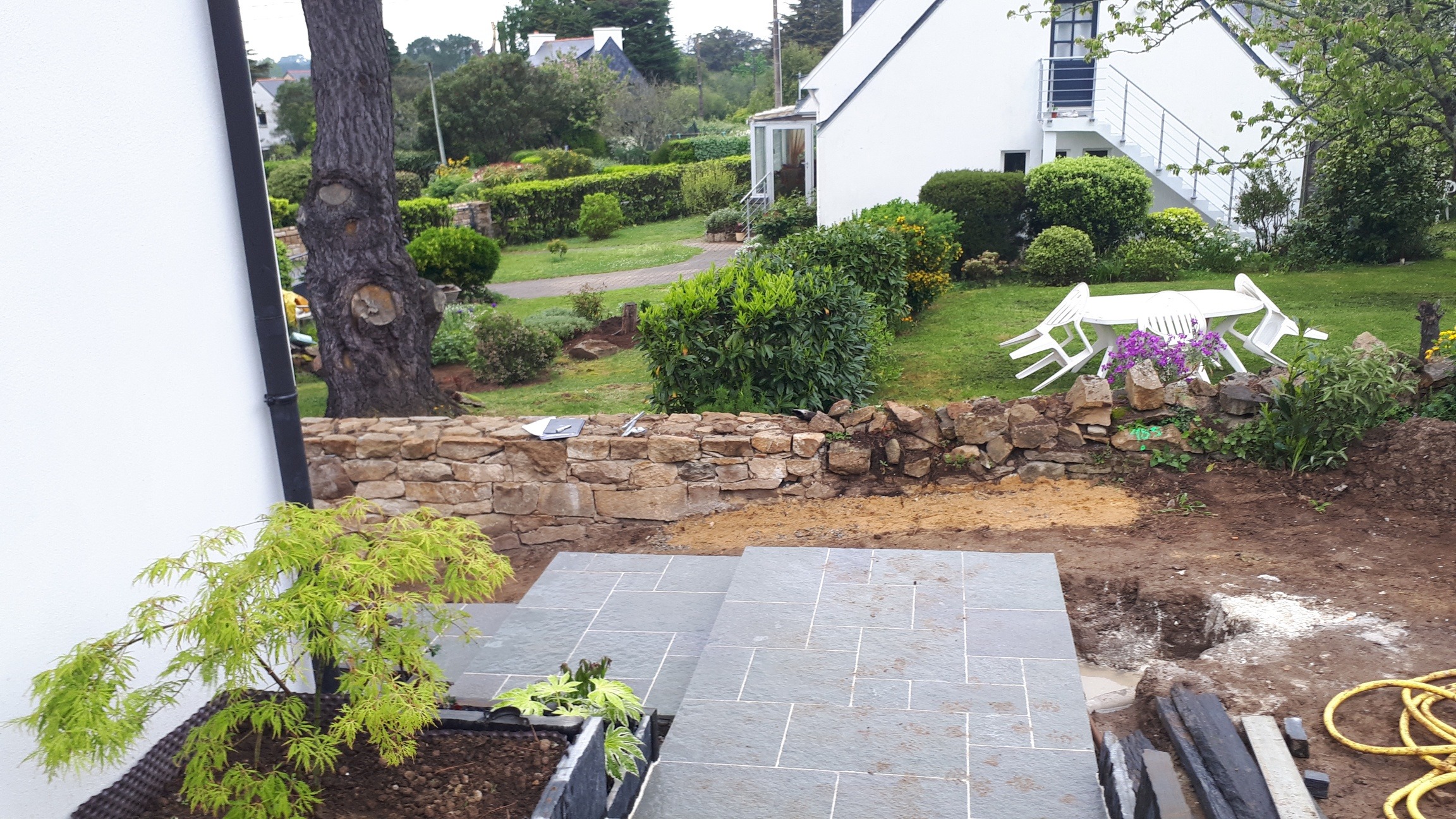 Terrasse en pierre naturelle en cours d'installation avec muret de pierres sèches dans un jardin du Morbihan