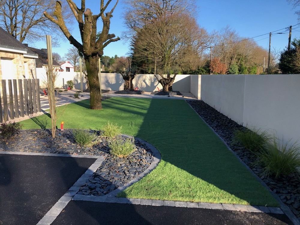 Jardin aménagé avec gazon synthétique, massifs de graminées et galets décoratifs près de Baden