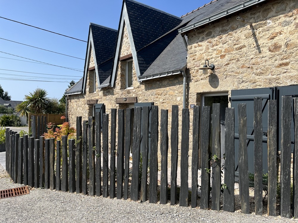 Clôture en bois brut devant une maison traditionnelle en pierre du Morbihan