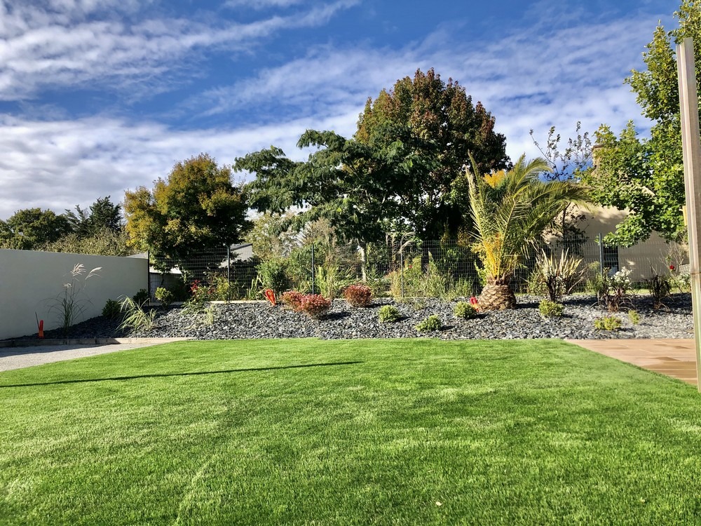 Jardin paysager avec pelouse verte, palmier et massifs de galets à l'approche de l'automne dans le Morbihan